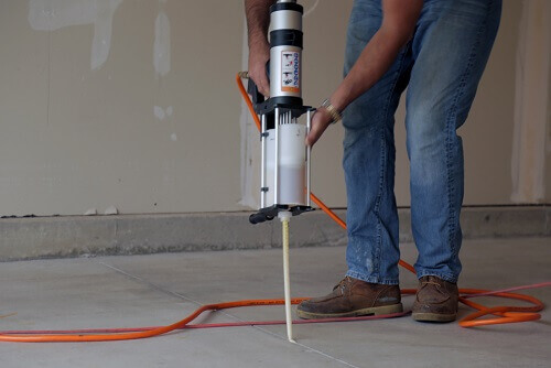 Person using crack filler on concrete floor with orange cord