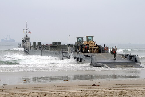 Large navy ship unloading construction vehicles onto beach