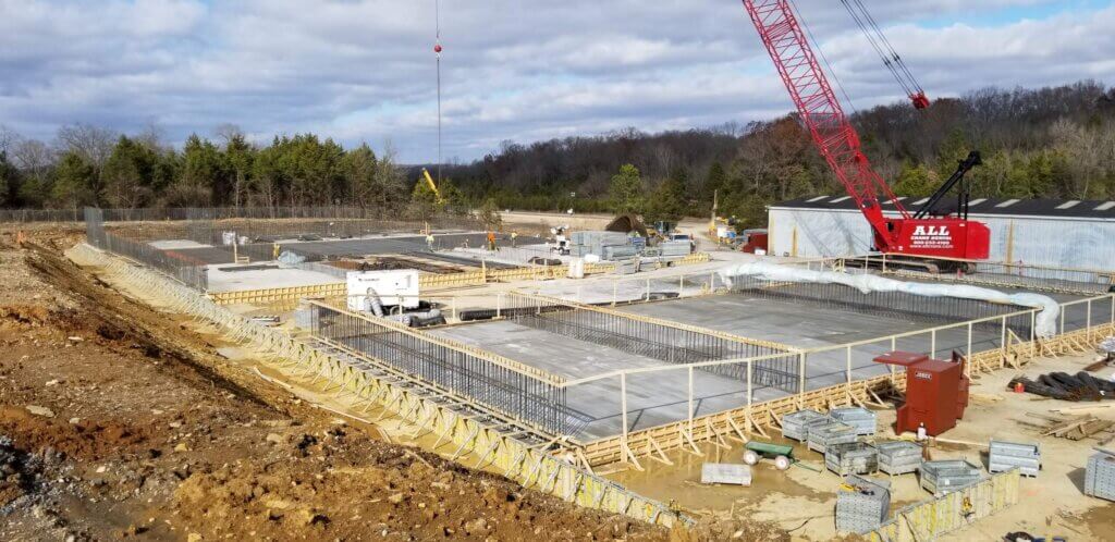 Large building site under construction with red crane and woods in backgroun